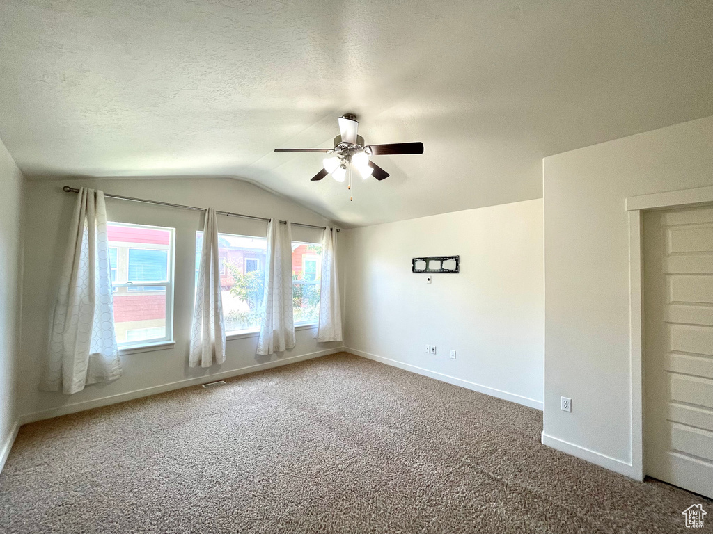 Carpeted empty room featuring a ceiling fan and vaulted ceiling