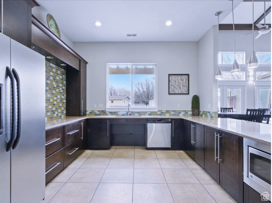Kitchen with appliances with stainless steel finishes, light countertops, light tile patterned flooring, decorative backsplash, and dark brown cabinetry