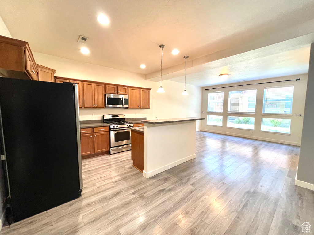 Kitchen featuring stainless steel appliances, light wood finished floors, open floor plan, brown cabinetry, and recessed lighting