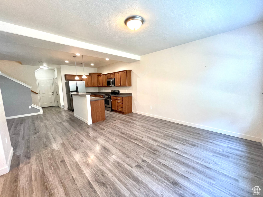 Kitchen featuring appliances with stainless steel finishes, open floor plan, wood finished floors, a kitchen island, and a textured ceiling