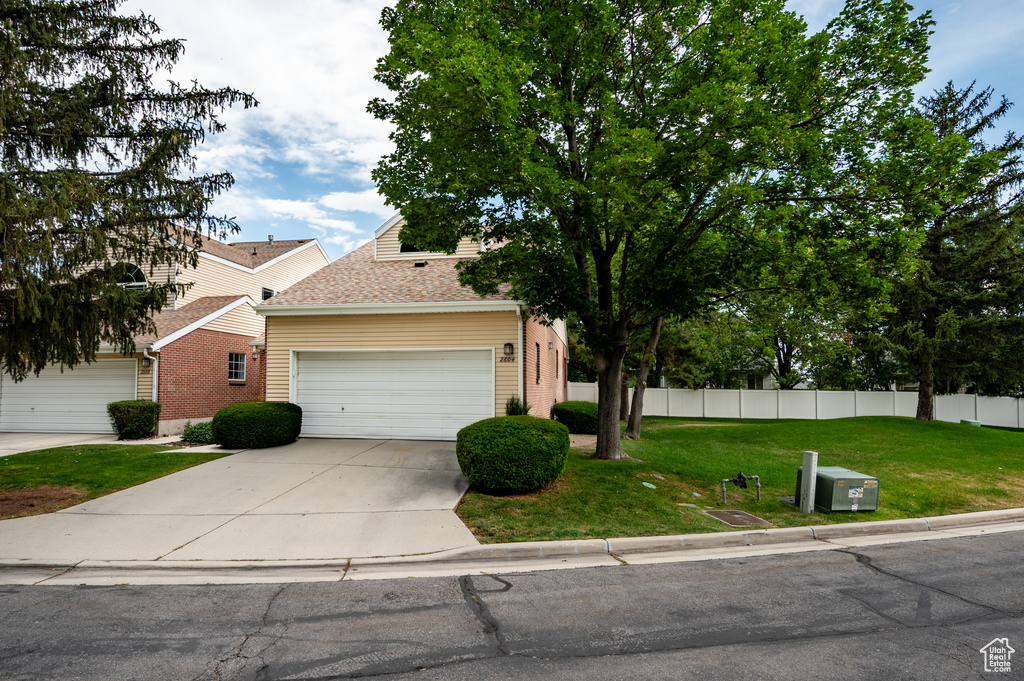 View of property hidden behind natural elements with an attached garage, driveway, and roof with shingles