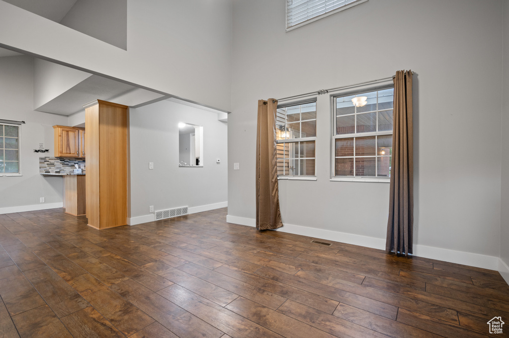 Unfurnished living room featuring a high ceiling, dark wood-style floors, and plenty of natural light