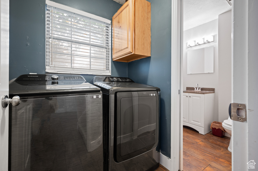 Washroom with cabinet space, washing machine and clothes dryer, and wood finished floors