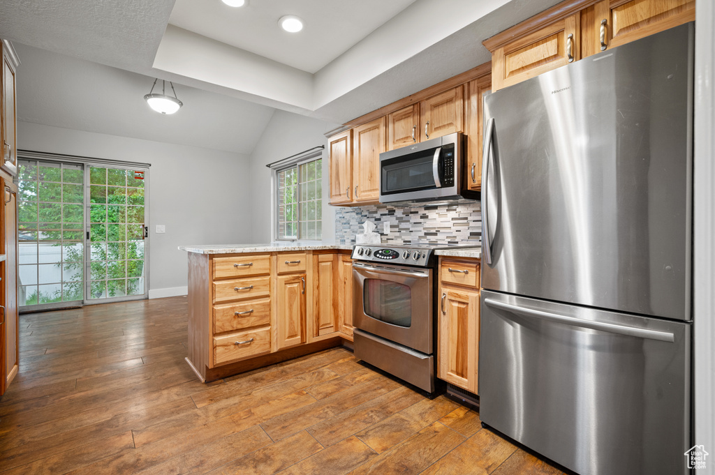 Kitchen featuring stainless steel appliances, a peninsula, lofted ceiling, wood-type flooring, and tasteful backsplash
