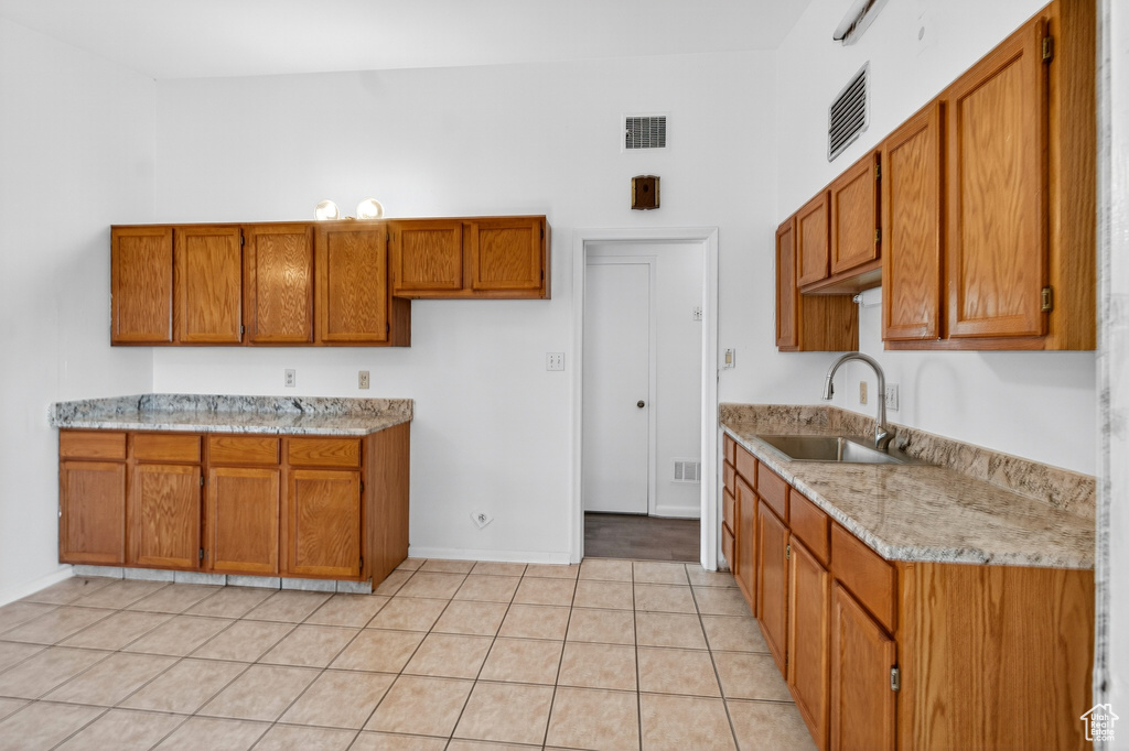 Kitchen with brown cabinets, light tile patterned flooring, and light stone counters