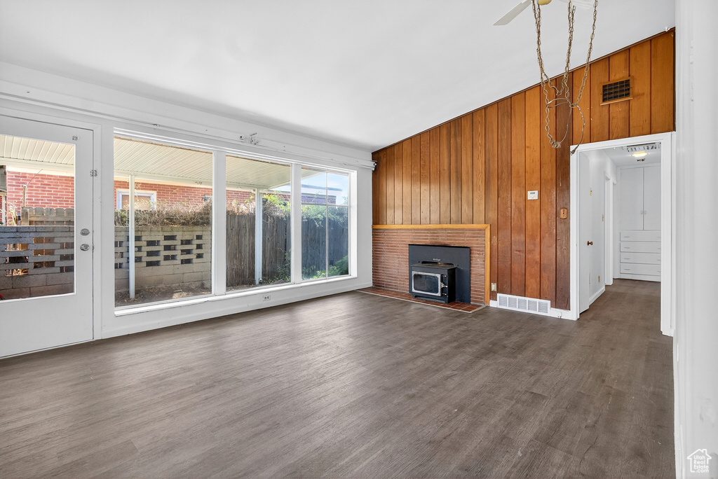 Unfurnished living room featuring wood walls, wood finished floors, a wood stove, and ceiling fan