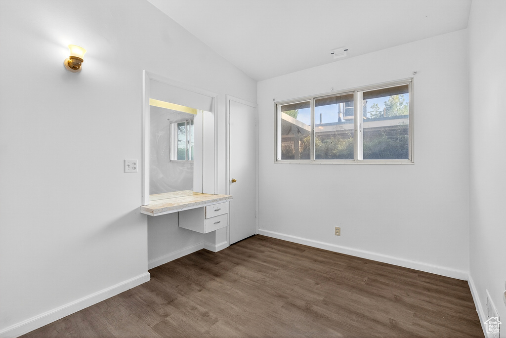 Unfurnished bedroom featuring dark wood-type flooring, built in desk, and vaulted ceiling