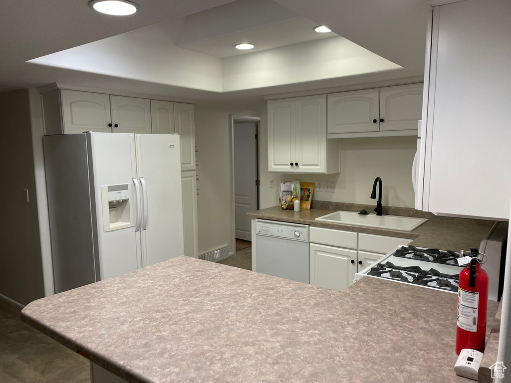 Kitchen featuring white appliances, a raised ceiling, a peninsula, and recessed lighting