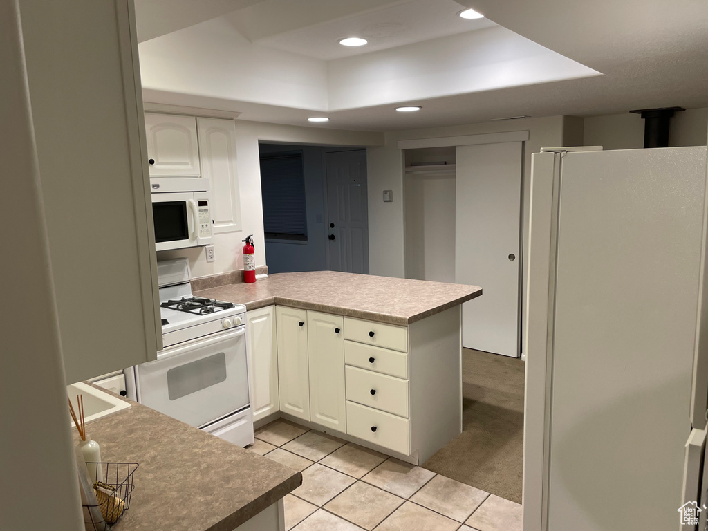 Kitchen featuring white appliances, a raised ceiling, a peninsula, light tile patterned floors, and recessed lighting