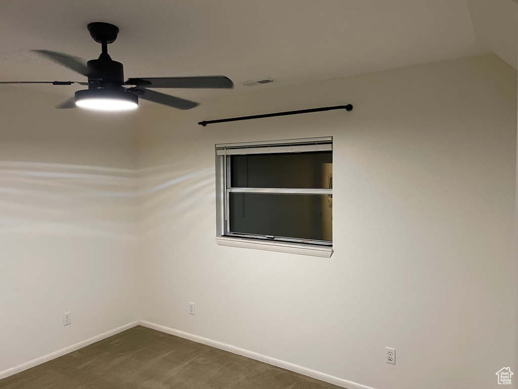 Spare room featuring a ceiling fan and dark colored carpet