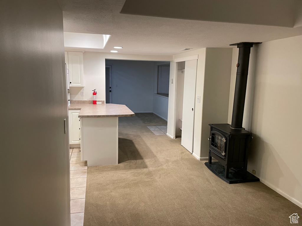 Below grade area with light carpet, a wood stove, and a textured ceiling