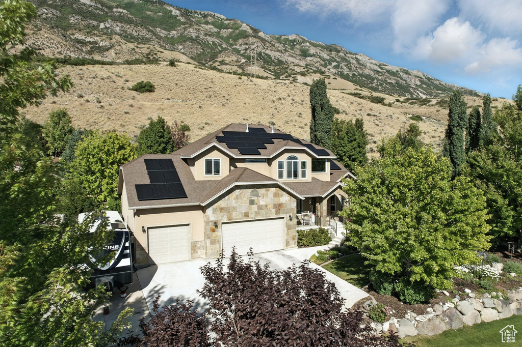 View of front of property featuring stone siding, roof mounted solar panels, driveway, an attached garage, and stucco siding