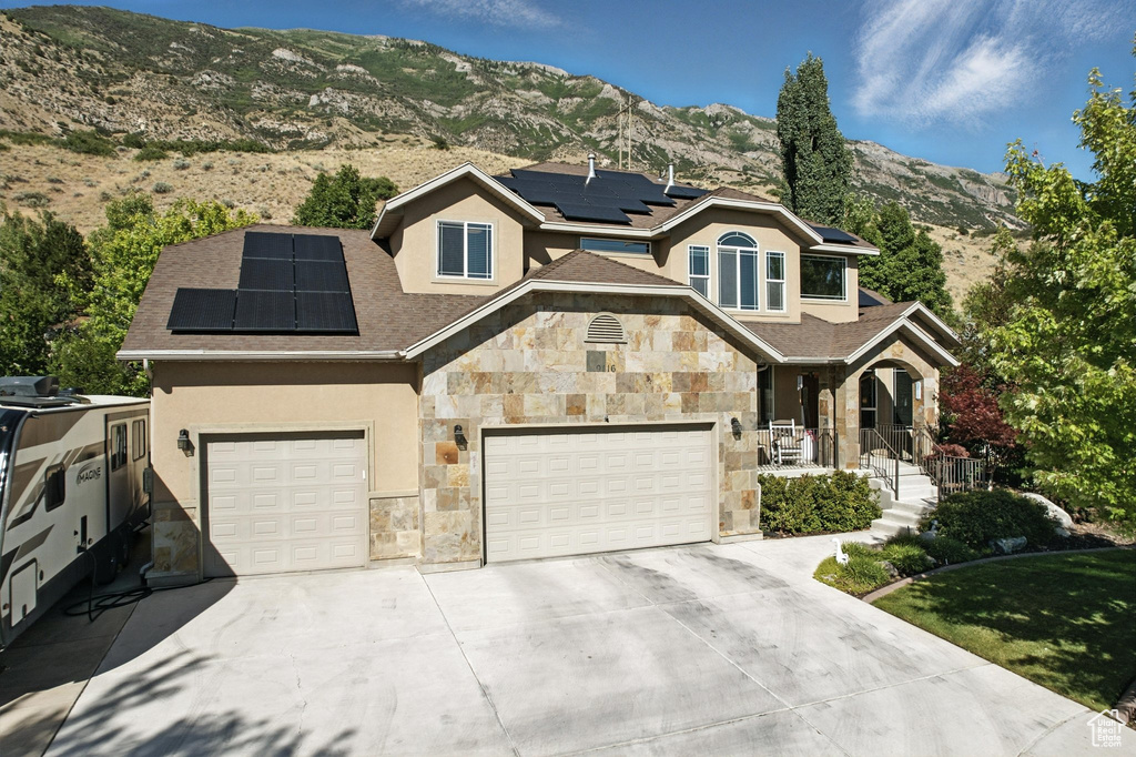 View of front facade with stone siding, solar panels, concrete driveway, stucco siding, and a mountain view