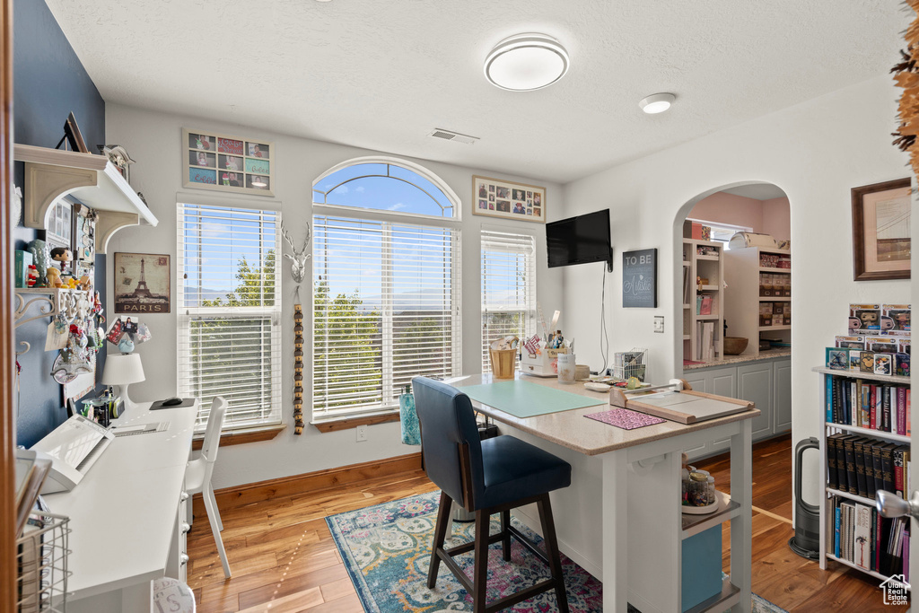 Office area with light wood-style floors, arched walkways, and a textured ceiling