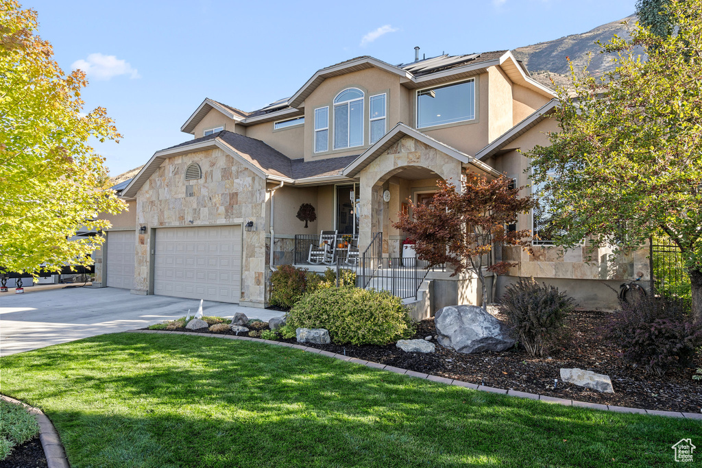 View of front of property with stone siding, stucco siding, roof mounted solar panels, concrete driveway, and an attached garage