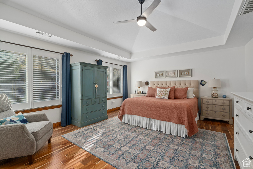 Bedroom featuring wood finished floors, vaulted ceiling, ceiling fan, and a tray ceiling