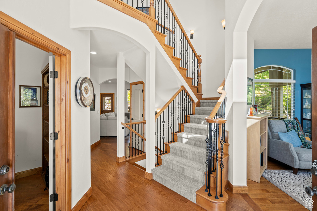 Stairway featuring wood finished floors, arched walkways, a high ceiling, and recessed lighting