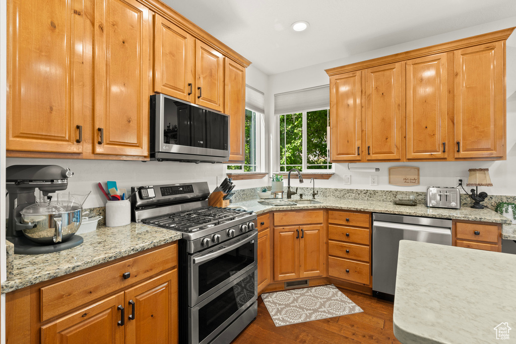 Kitchen featuring stainless steel appliances, dark wood-style flooring, light stone counters, and recessed lighting