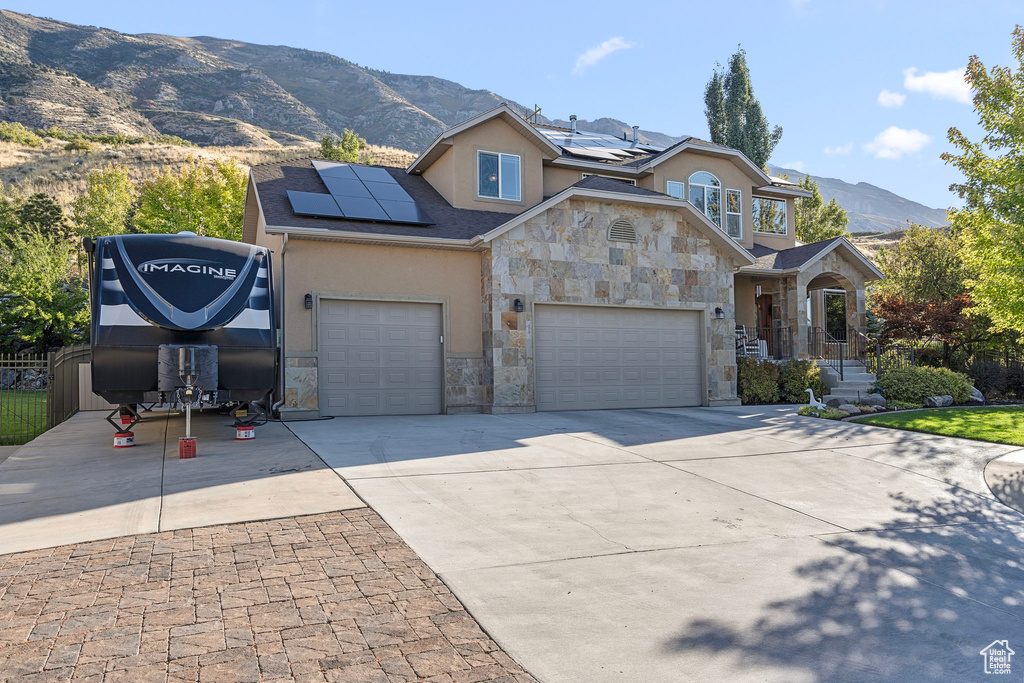 View of front of property featuring stone siding, stucco siding, a mountain view, driveway, and solar panels