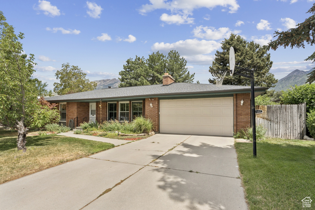 Single story home with an attached garage, brick siding, driveway, and a mountain view