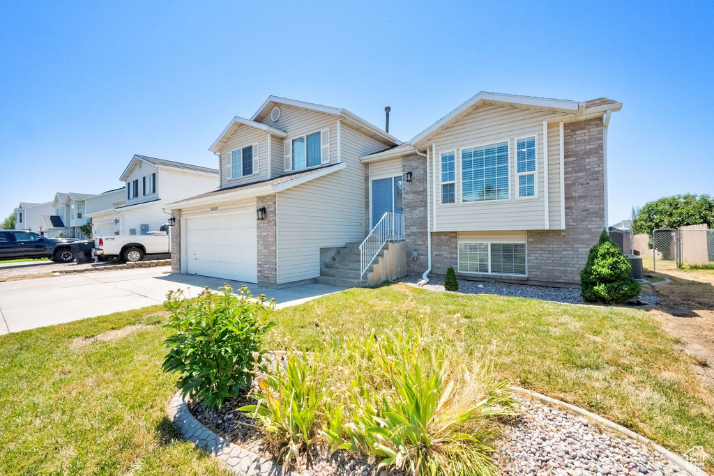 Tri-level home featuring brick siding, driveway, a garage, and a front lawn