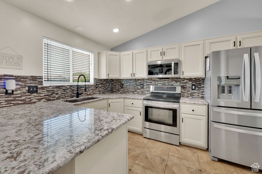 Kitchen with appliances with stainless steel finishes, lofted ceiling, backsplash, light stone countertops, and white cabinetry