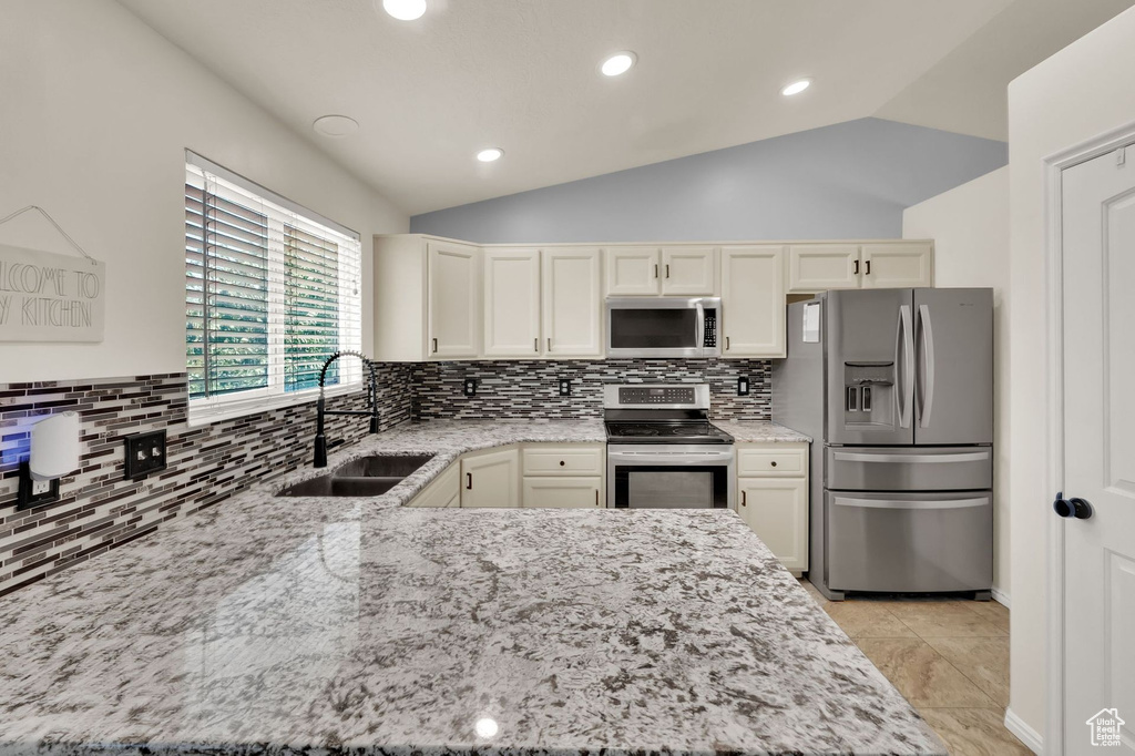 Kitchen featuring appliances with stainless steel finishes, vaulted ceiling, light stone countertops, decorative backsplash, and recessed lighting