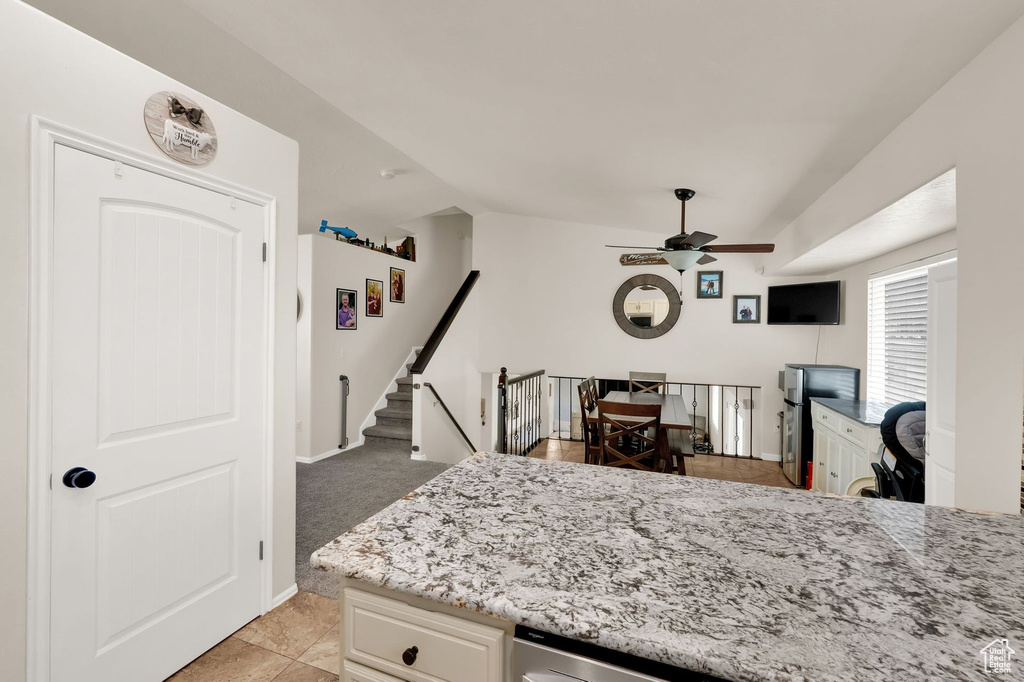 Kitchen with ceiling fan, vaulted ceiling, light stone countertops, light tile patterned floors, and white cabinetry