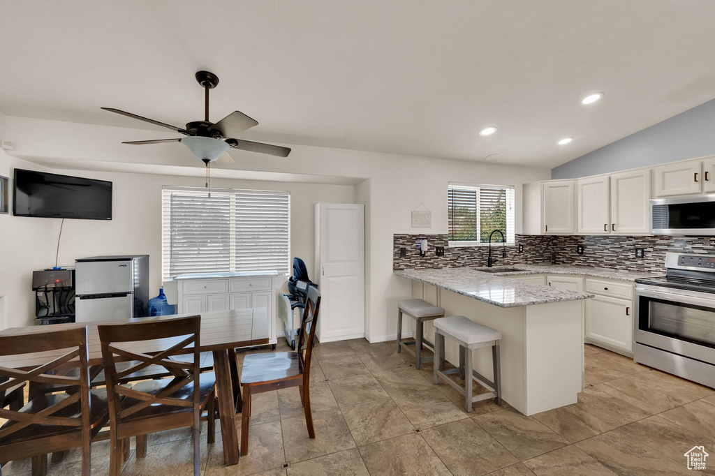 Kitchen with appliances with stainless steel finishes, a peninsula, tasteful backsplash, white cabinets, and light stone countertops
