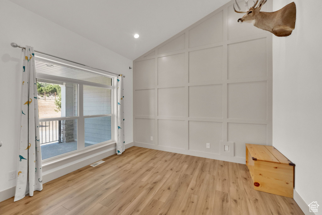 Empty room with a decorative wall, light wood finished floors, lofted ceiling, and recessed lighting