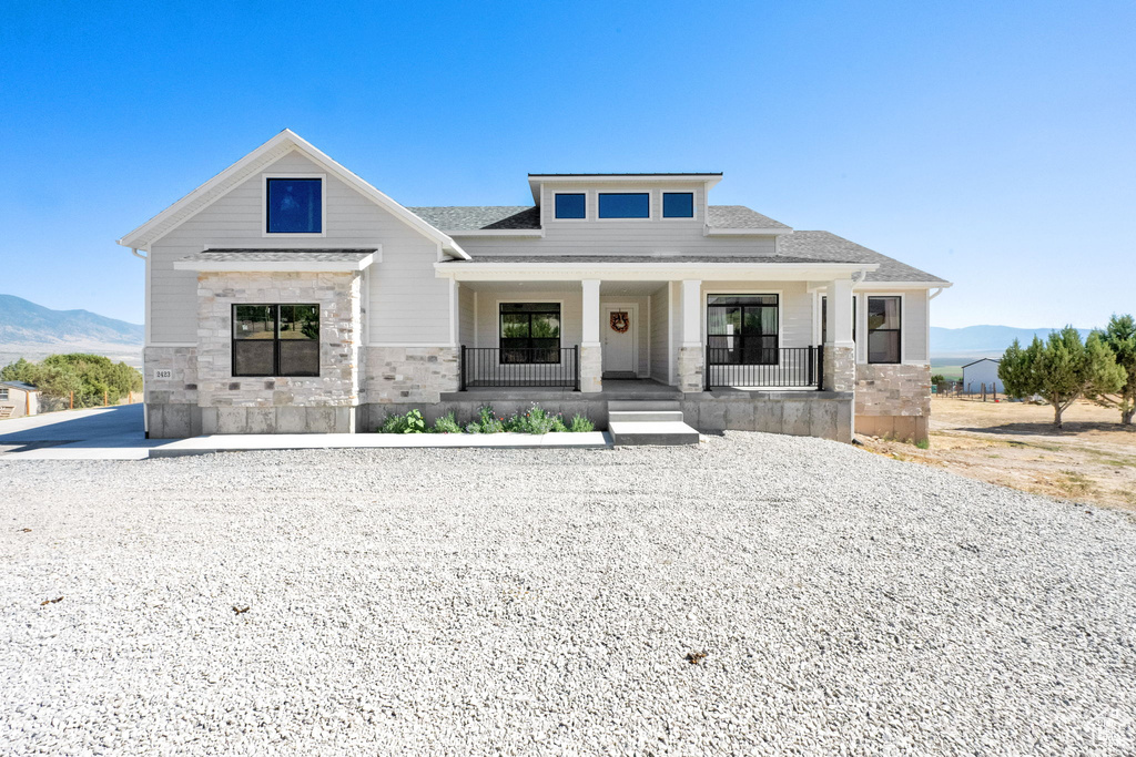View of front of property featuring a mountain view, stone siding, a porch, and a shingled roof