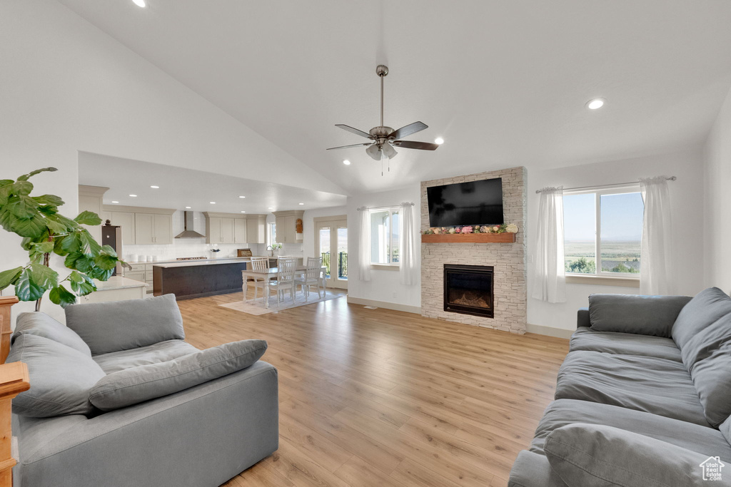 Living room featuring recessed lighting, ceiling fan, a stone fireplace, light wood-style floors, and high vaulted ceiling