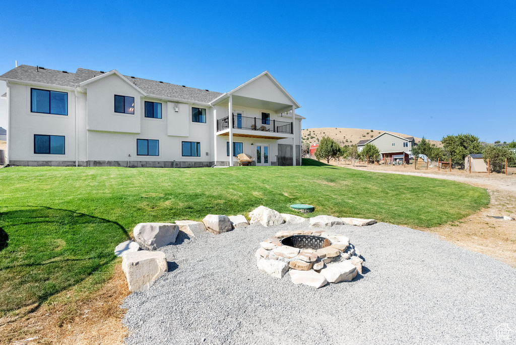 Back of house featuring a balcony, a fire pit, a lawn, and stucco siding