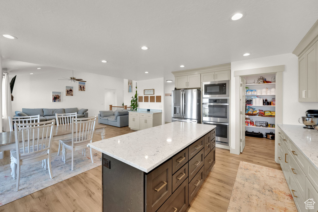 Kitchen with appliances with stainless steel finishes, open floor plan, light wood-style flooring, a kitchen island, and light stone counters
