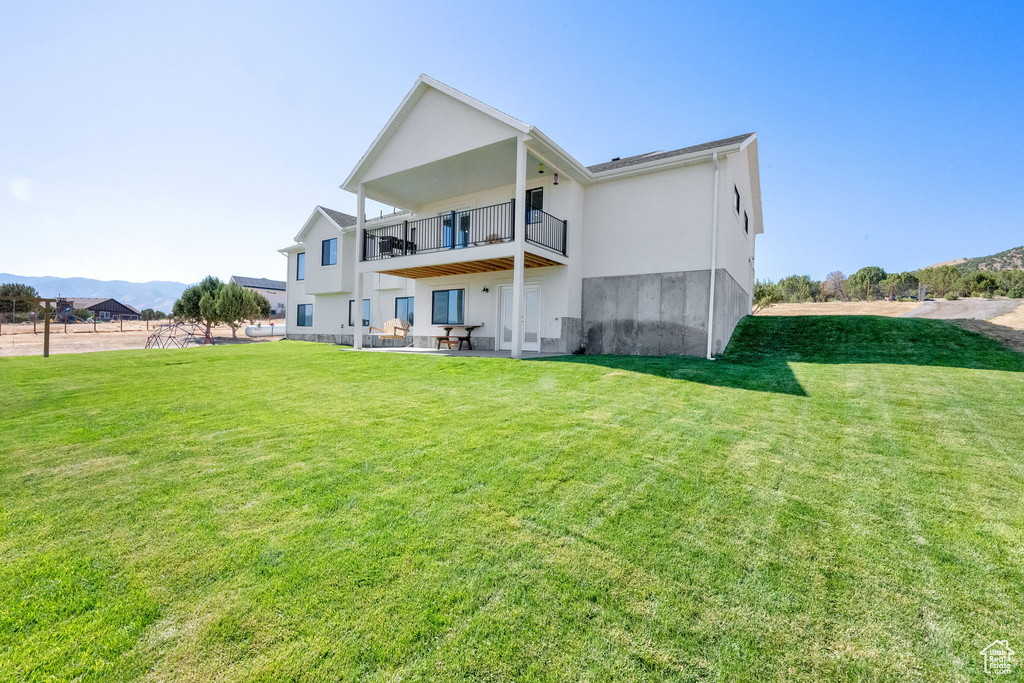 Back of property featuring a balcony, a yard, a patio area, and stucco siding