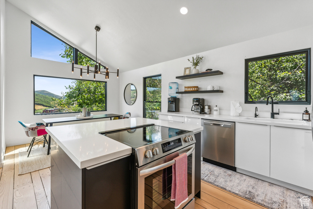 Kitchen with stainless steel appliances, light wood-style floors, light countertops, white cabinets, and high vaulted ceiling
