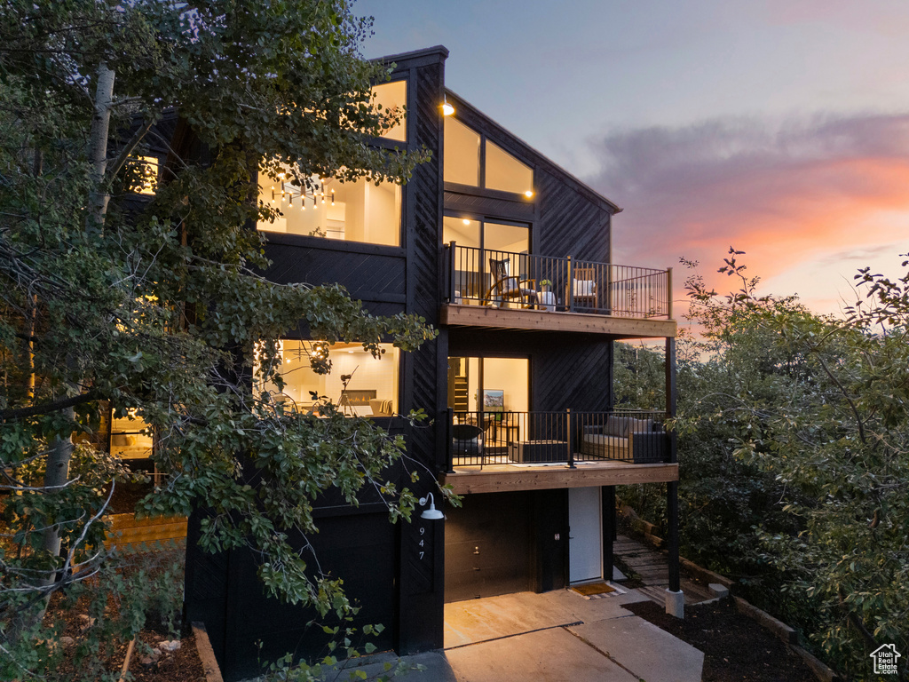 Back of house with a balcony, an attached garage, and concrete driveway