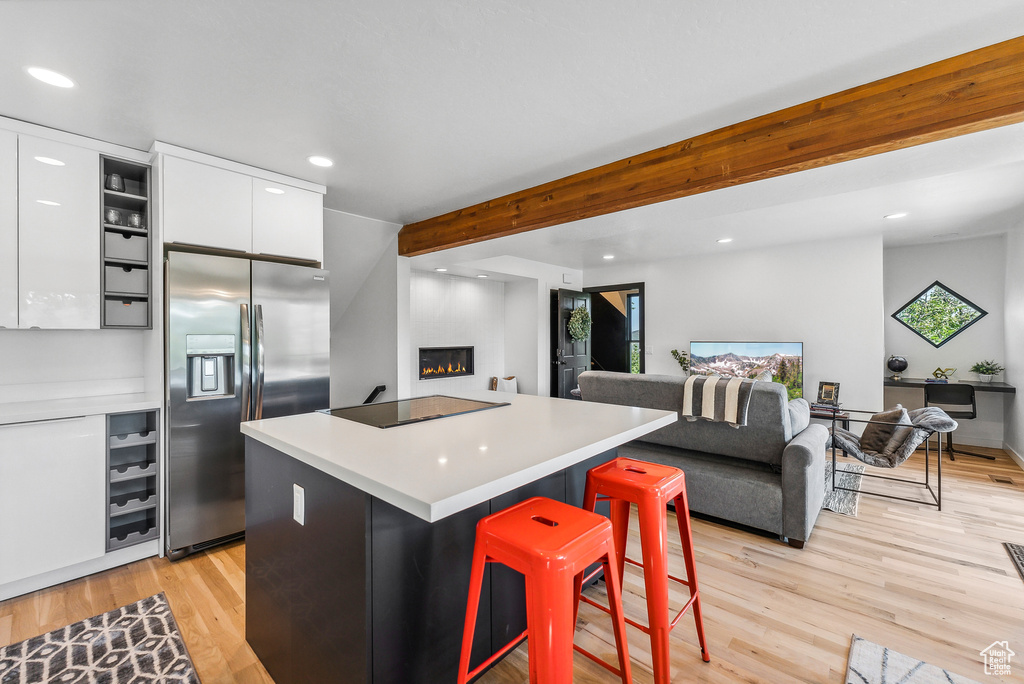 Kitchen featuring stainless steel fridge with ice dispenser, black electric cooktop, recessed lighting, white cabinets, and a fireplace