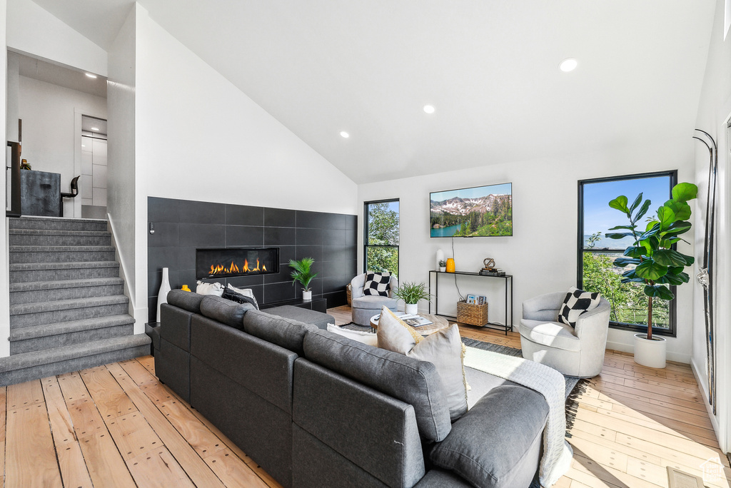 Living area featuring high vaulted ceiling, light wood-style flooring, recessed lighting, a fireplace, and stairs