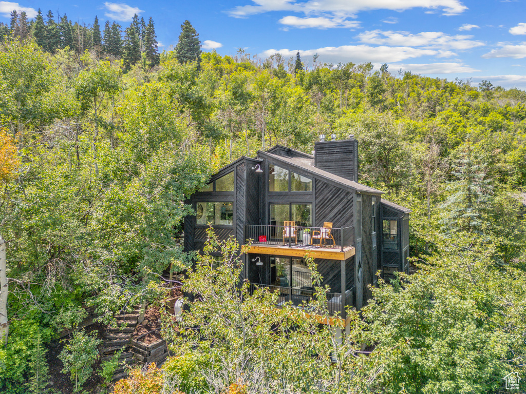 Rear view of house with a forest view, a chimney, and a wooden deck