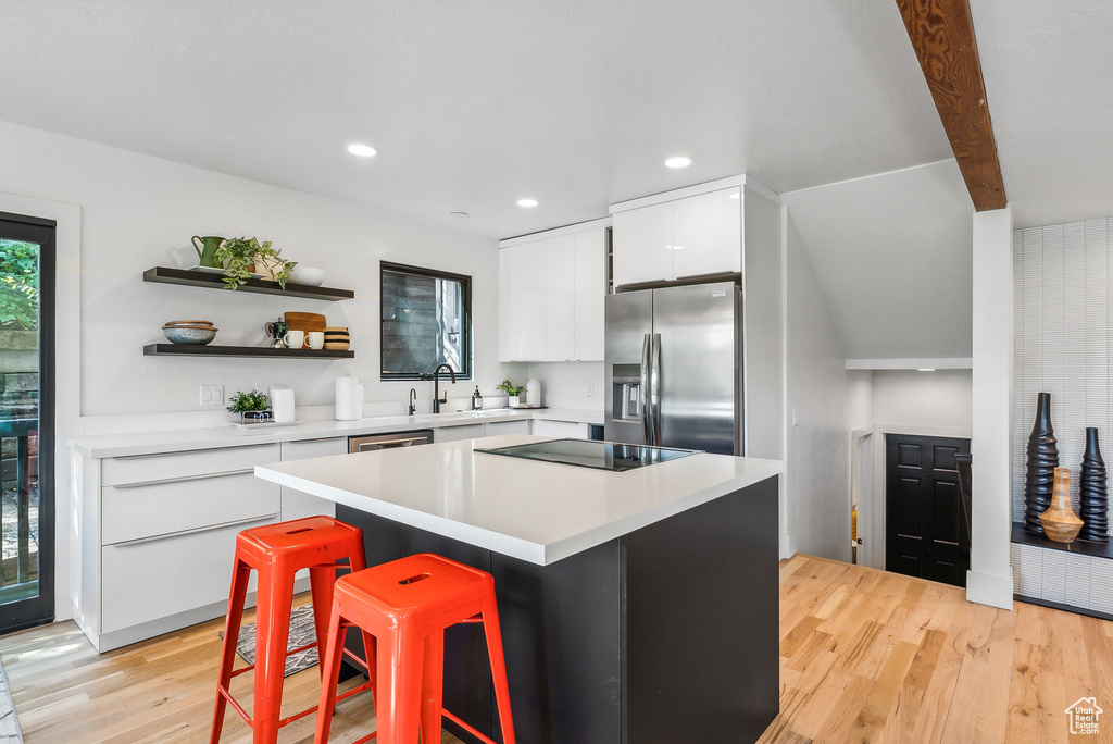 Kitchen with stainless steel refrigerator with ice dispenser, light wood-style floors, white cabinets, a kitchen breakfast bar, and light countertops