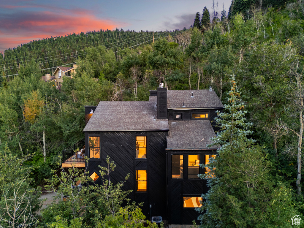 Rear view of property featuring a balcony, a forest view, a chimney, and a shingled roof