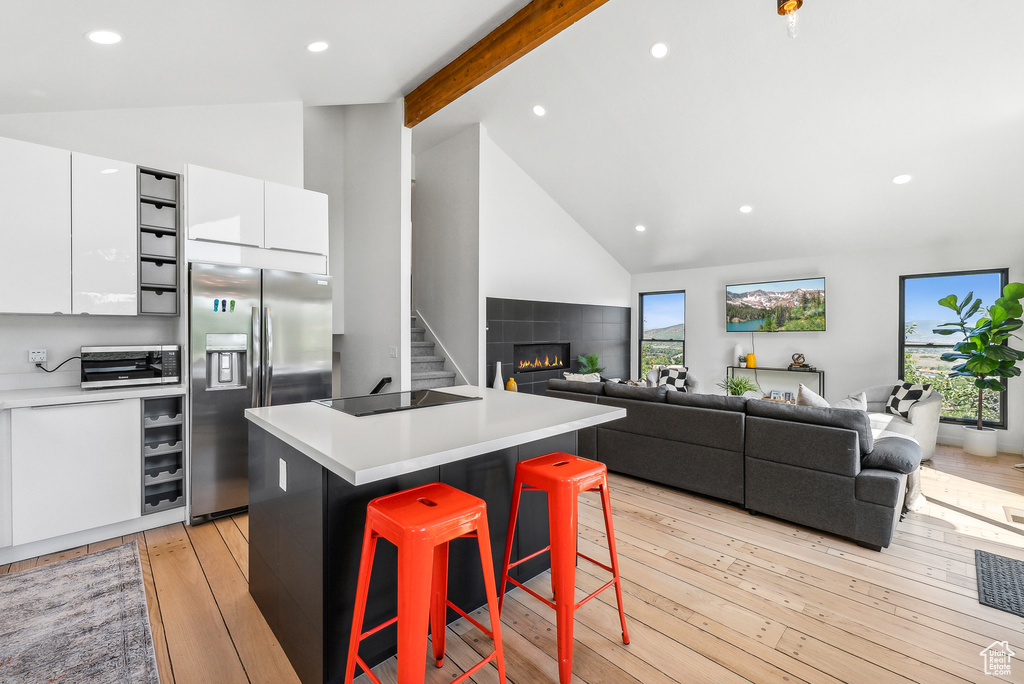 Kitchen with stainless steel refrigerator with ice dispenser, white cabinetry, a kitchen bar, high vaulted ceiling, and a center island