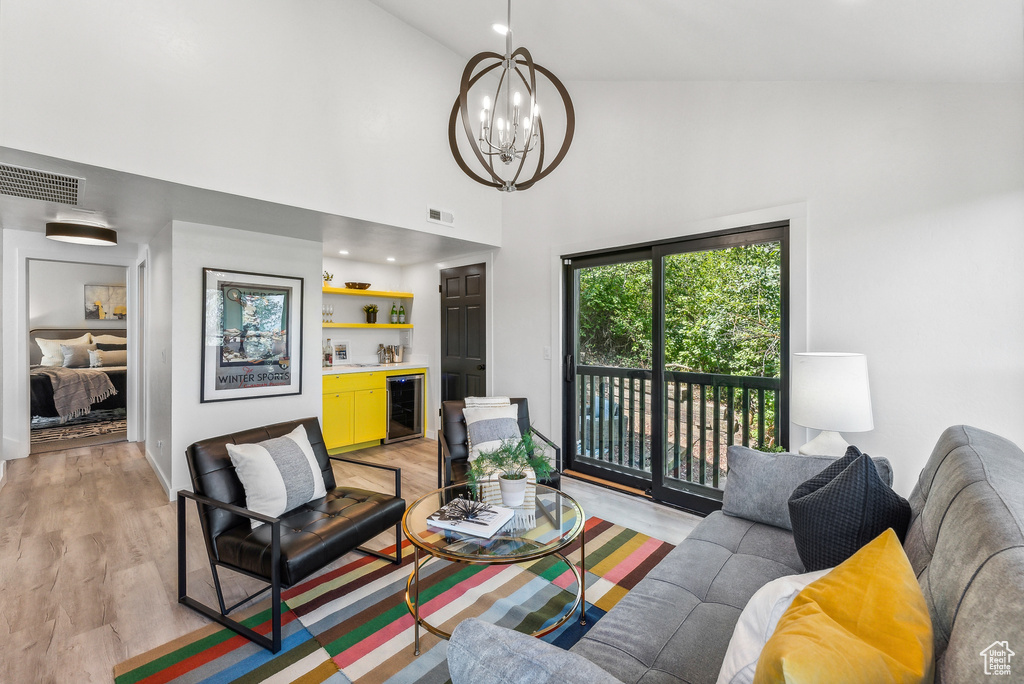 Living room featuring beverage cooler, a chandelier, light wood-type flooring, a towering ceiling, and bar area