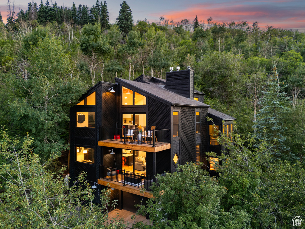 Back of property at dusk with a chimney and a balcony