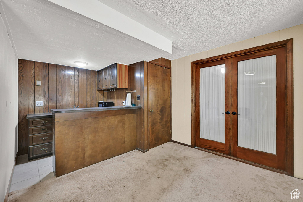 Kitchen with french doors, light carpet, a textured ceiling, wooden walls, and brown cabinetry
