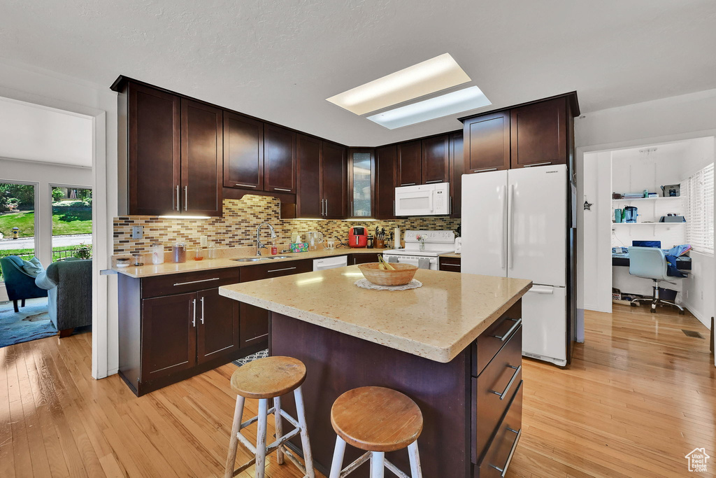 Kitchen with white appliances, light wood-type flooring, decorative backsplash, and dark brown cabinets