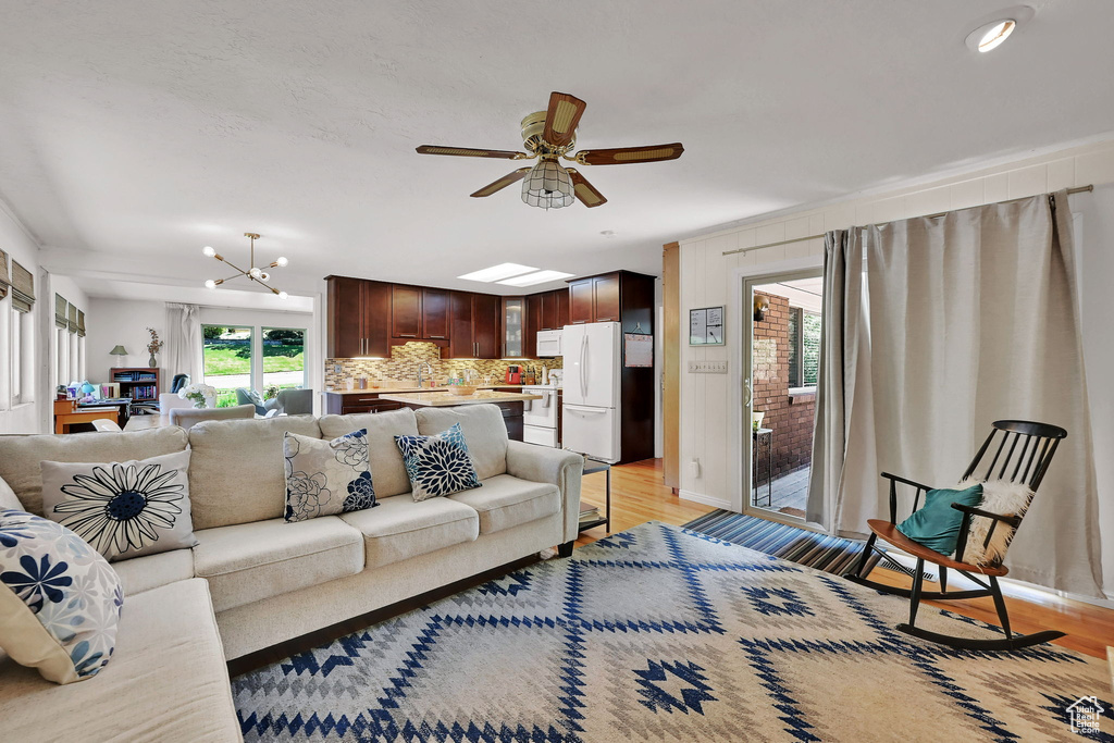 Living area with light wood-style floors, ceiling fan, and a chandelier