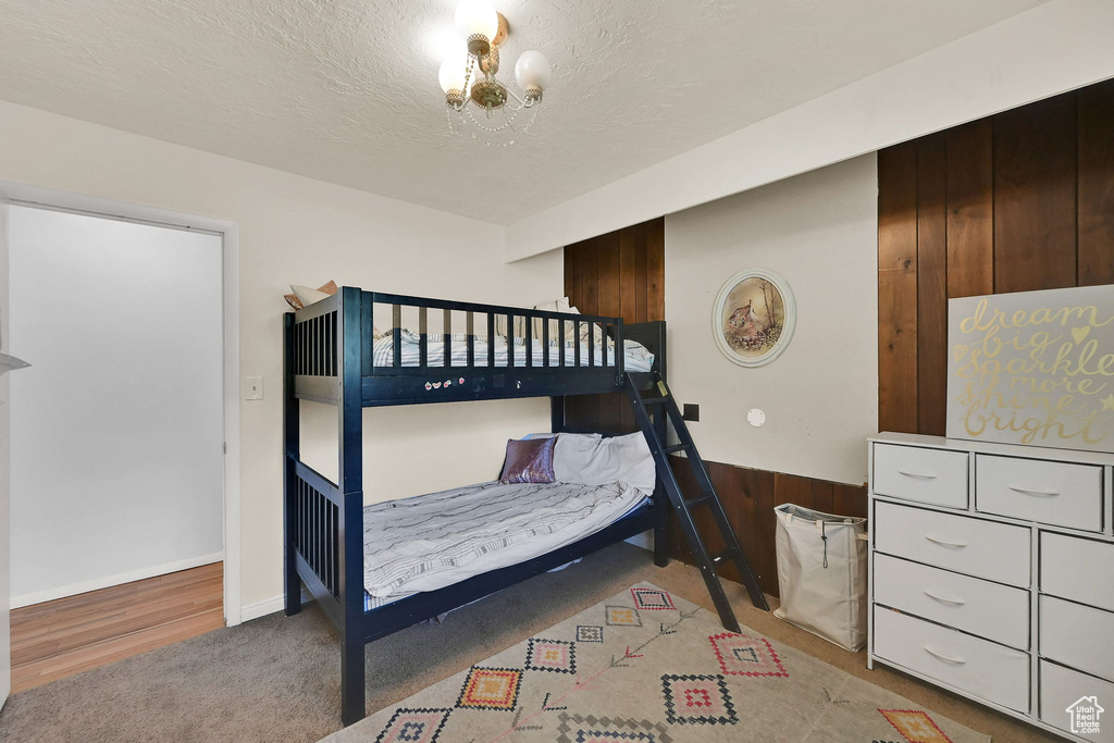 Bedroom featuring carpet, a textured ceiling, a chandelier, and wooden walls