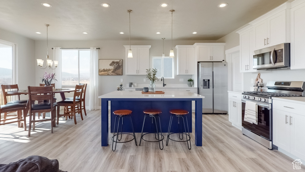 Kitchen featuring appliances with stainless steel finishes, a center island, light wood finished floors, a kitchen bar, and recessed lighting